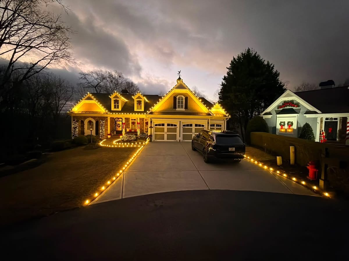 Professional warm-white roofline and driveway Christmas light installation on a two-story home at dusk